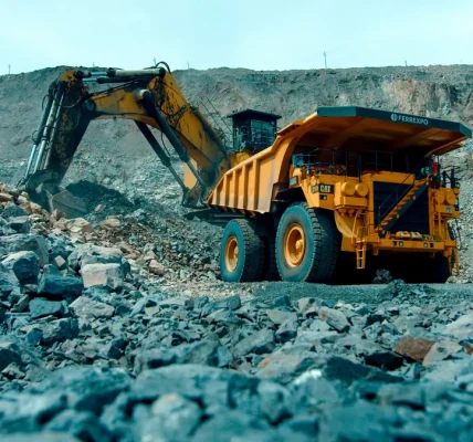 Жовтий кар’єрний самоскид Ferrexpo і екскаватор серед каміння на відкритому кар’єрі