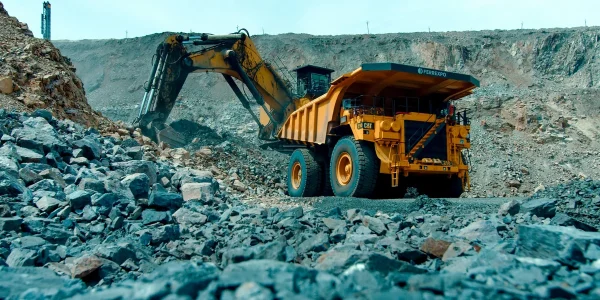 Жовтий кар’єрний самоскид Ferrexpo і екскаватор серед каміння на відкритому кар’єрі