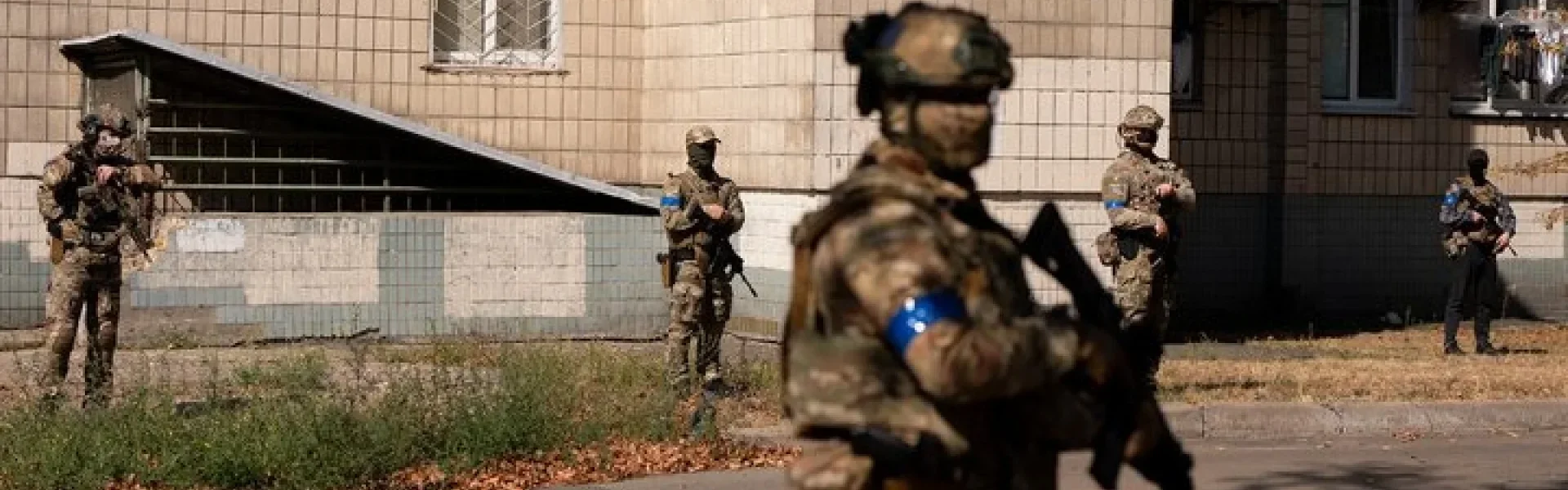 Військові в камуфляжі з синіми пов’язками біля будівлі на вулиці