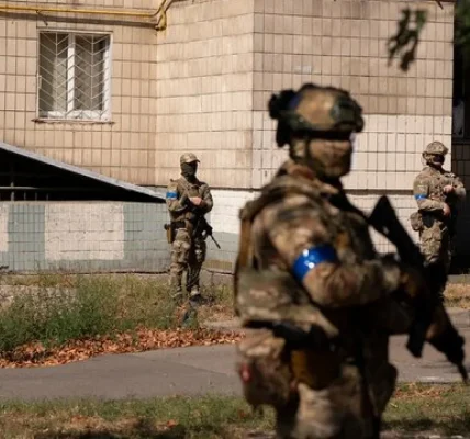Військові в камуфляжі з синіми пов’язками біля будівлі на вулиці