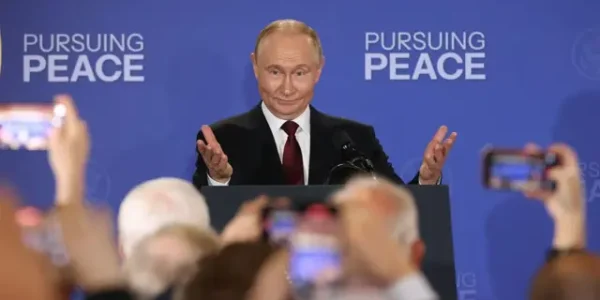 Путін за трибуною з піднятими руками на тлі напису Pursuing Peace