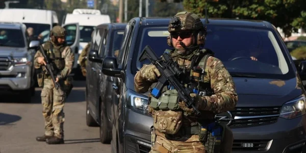 Військові в камуфляжі з автоматами біля сірого мікроавтобуса на вулиці
