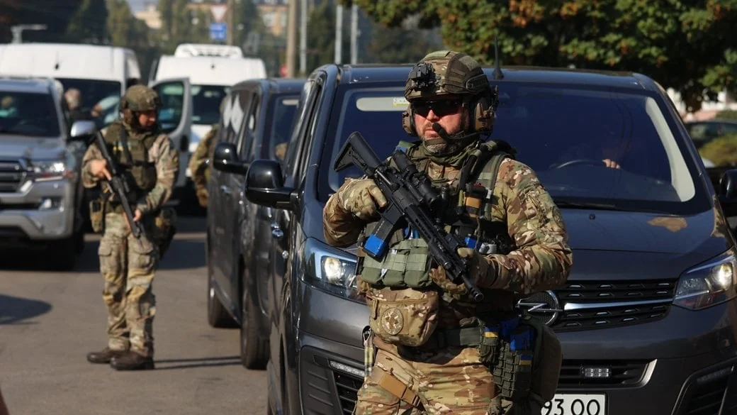 Військові в камуфляжі з автоматами біля сірого мікроавтобуса на вулиці