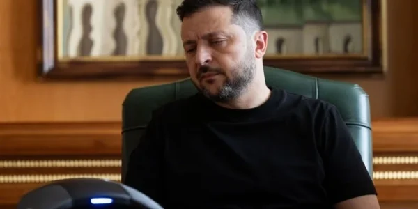 Зеленський у чорній футболці сидить за столом у зеленому кріслі кабінету