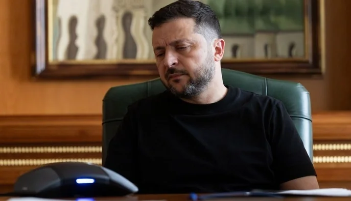Зеленський у чорній футболці сидить за столом у зеленому кріслі кабінету