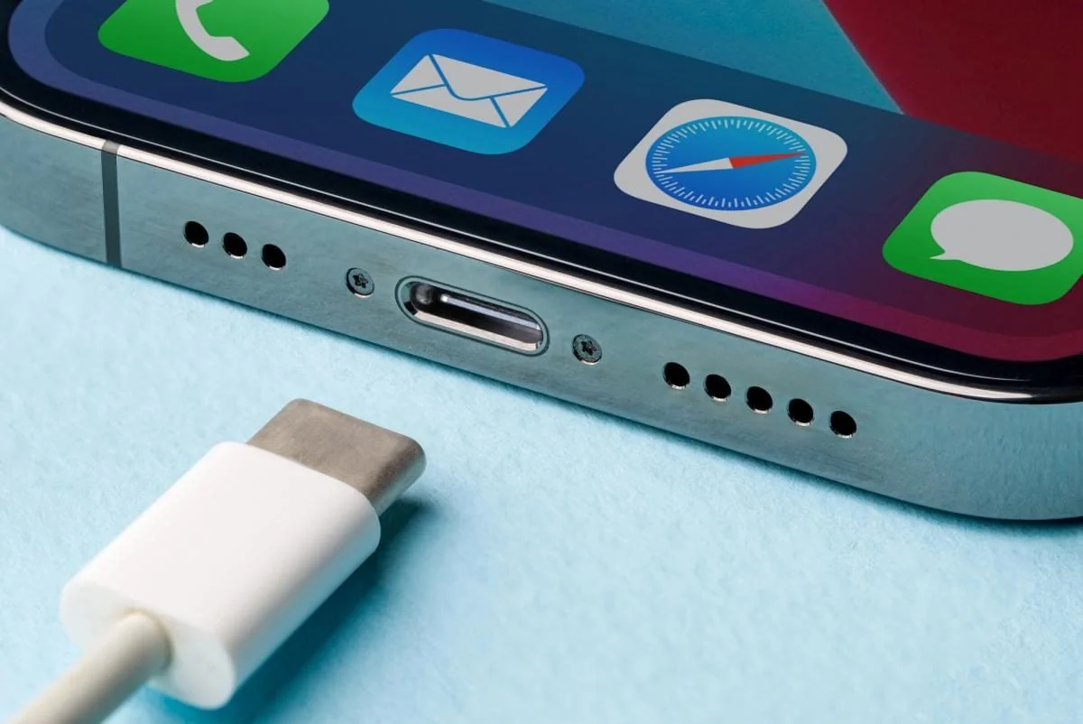 Нижня частина iPhone з портом USB-C і білим кабелем на блакитному тлі
