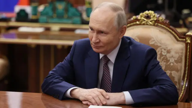 Володимир Путін у синьому костюмі сидить за столом у кабінеті