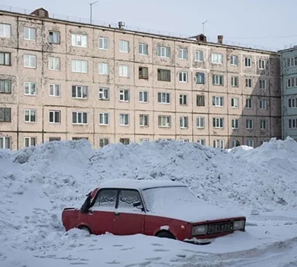 Червоний автомобіль засипаний снігом біля панельних багатоповерхівок взимку