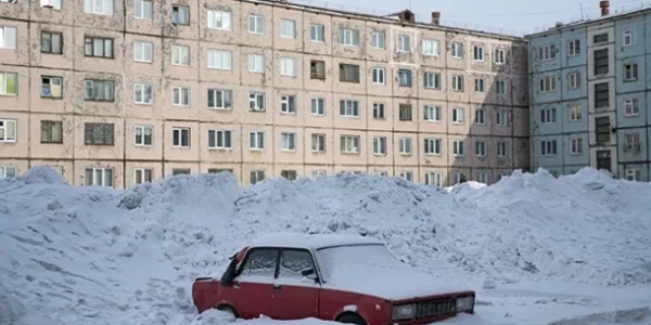 Червоний автомобіль засипаний снігом біля панельних багатоповерхівок взимку
