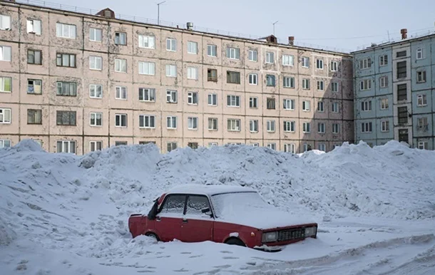 Червоний автомобіль засипаний снігом біля панельних багатоповерхівок взимку